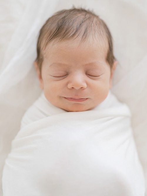 Smiling newborn baby wrapped in white fabric photographed in natural light